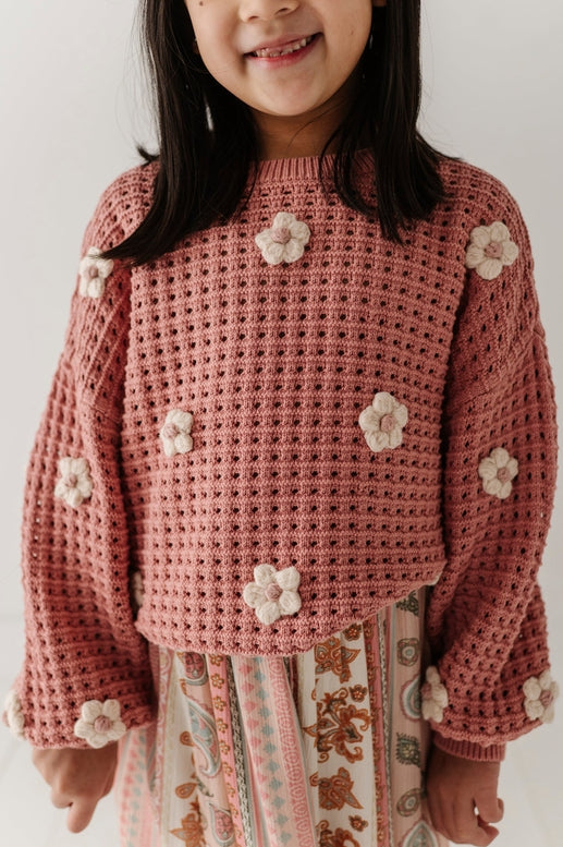 Child wearing a pink crochet sweater with flower patterns on a white background