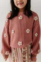 Child wearing a pink crochet sweater with flower patterns on a white background