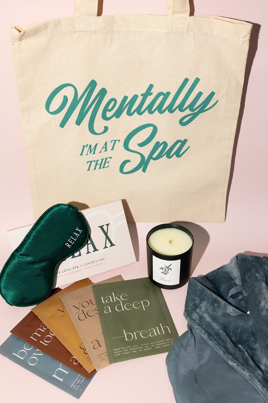Tote bag with 'Mentally I'm at the Spa' text, eye mask, candles, and books on a pink background