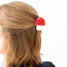 Red and white mushroom-shaped hair clip on a person's hair against a white background