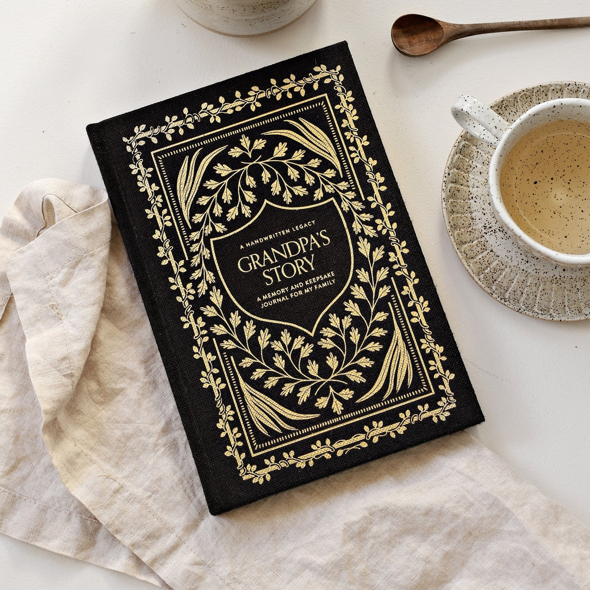 Decorative journal titled 'Grandma's Story' on a table with a cup of coffee and a spoon.