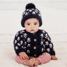 Baby wearing a navy cardigan with pink floral patterns and matching pants, sitting on a white surface.