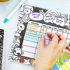 Hand holding a planner with a reward chart and stickers on a light blue background