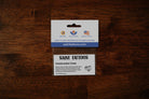 A small rectangular Saint Tattoos card or sticker package labeled 'Construction Crew' photographed from above on a dark wood surface.
