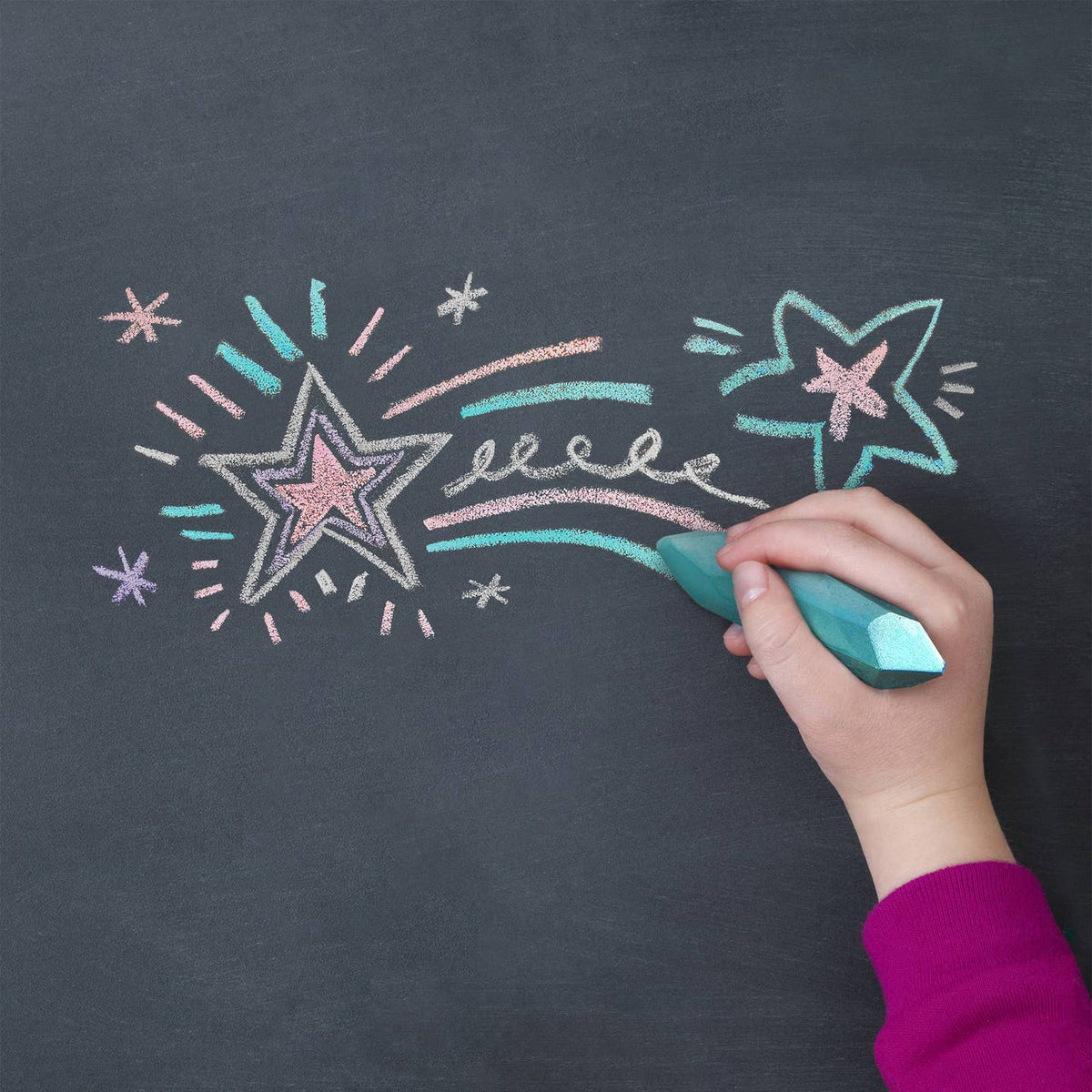 Hand drawing stars and a rainbow on a blackboard with colorful chalk.