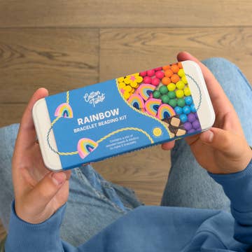 Person holding a rainbow bracelet making kit against a wooden floor background