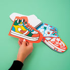 Colorful paper shoes held by a hand on a green background