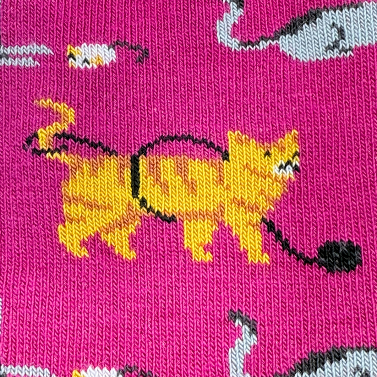 A close-up of a bright pink knit fabric with a repeating pattern of yellow cats and gray-and-white birds.
