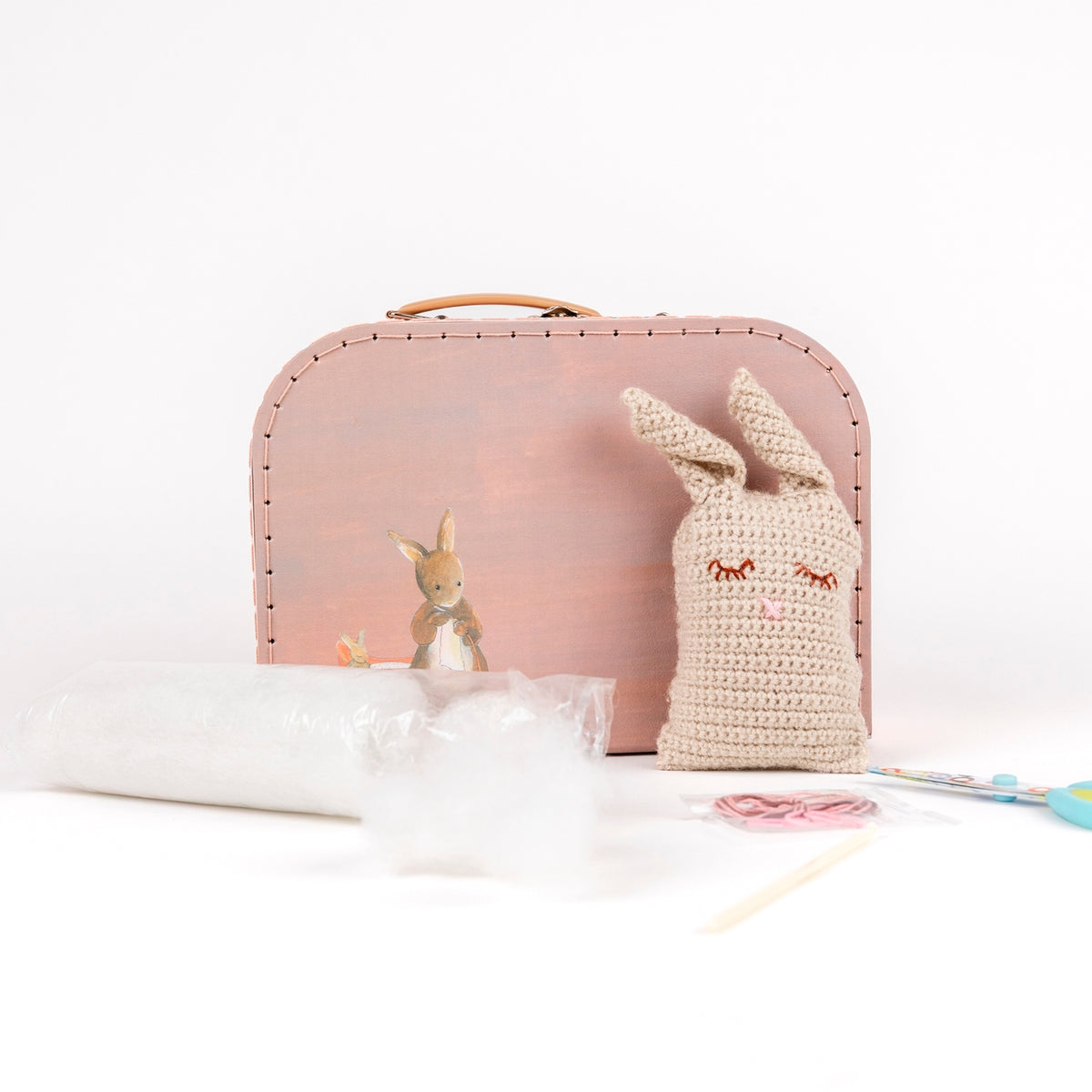 Pink suitcase with a small rabbit plush toy and a knitted hat on a white surface.