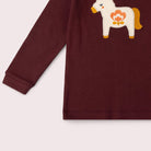A close-up of a long-sleeve burgundy children's sweatshirt featuring a white embroidered Dala horse with orange and yellow details on the chest, set against a light beige background.