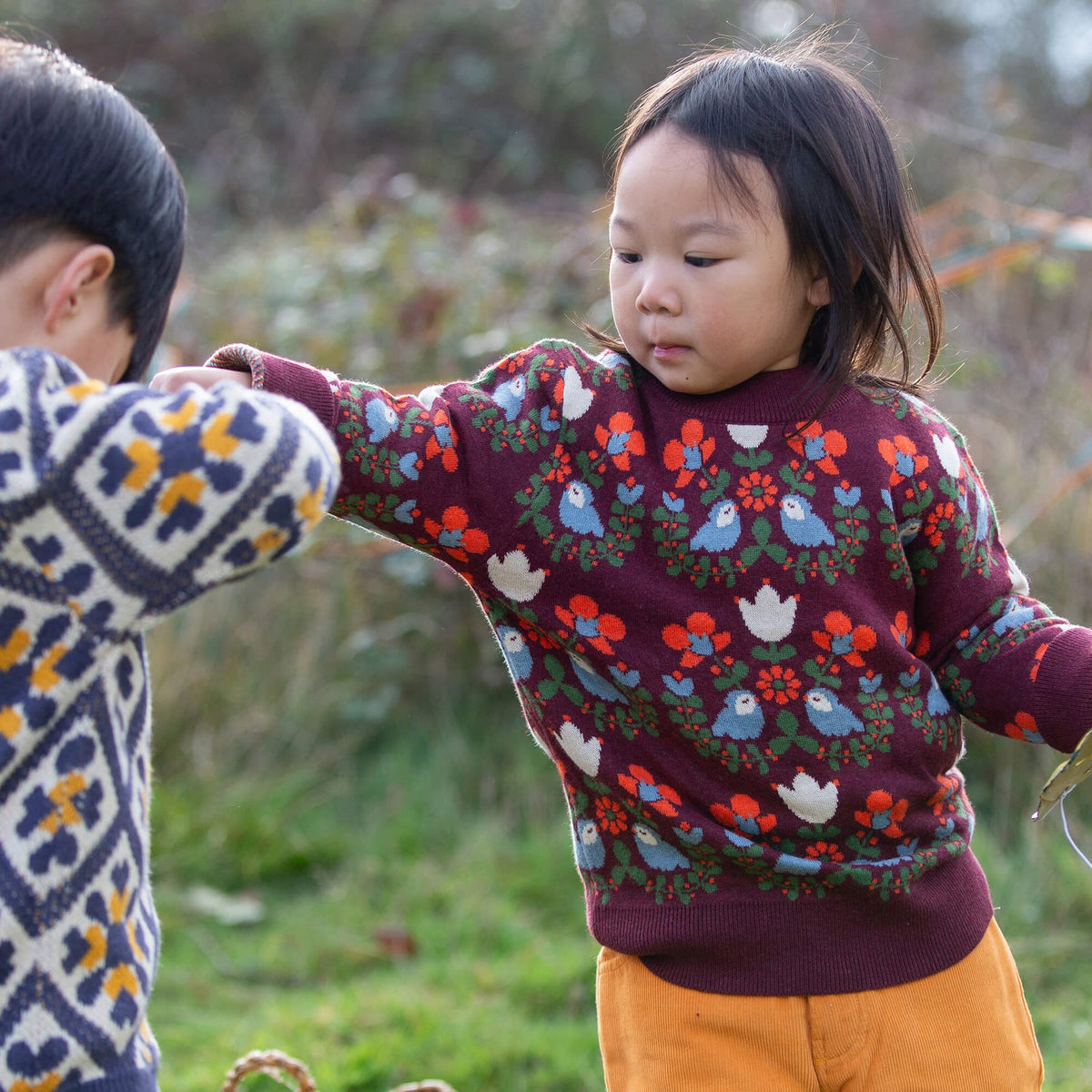 Two children wearing patterned sweaters outdoors in a natural setting
