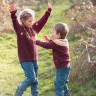 A young girl and boy wearing a patterned sweater with a blurred natural background