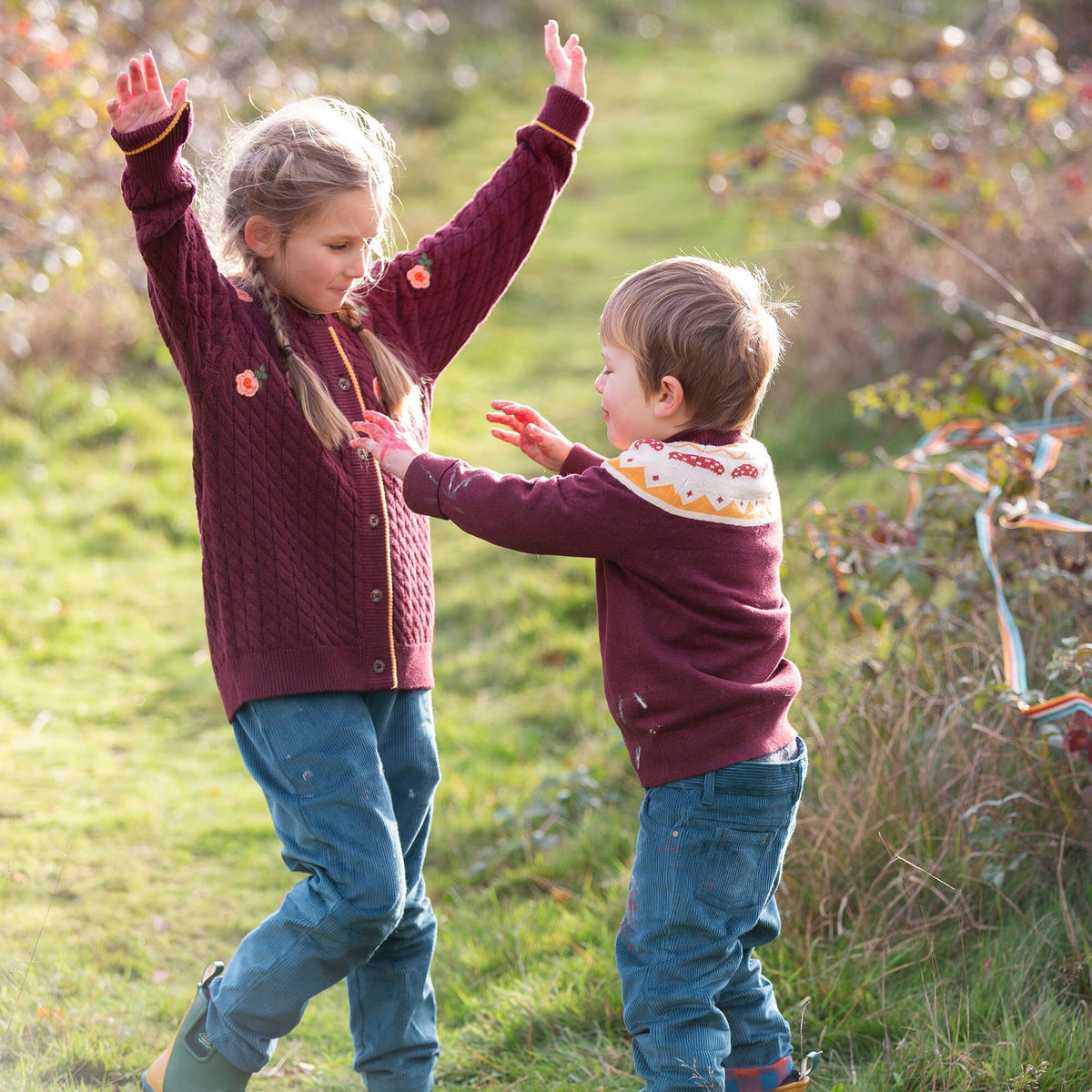 A young girl and boy wearing a patterned sweater with a blurred natural background