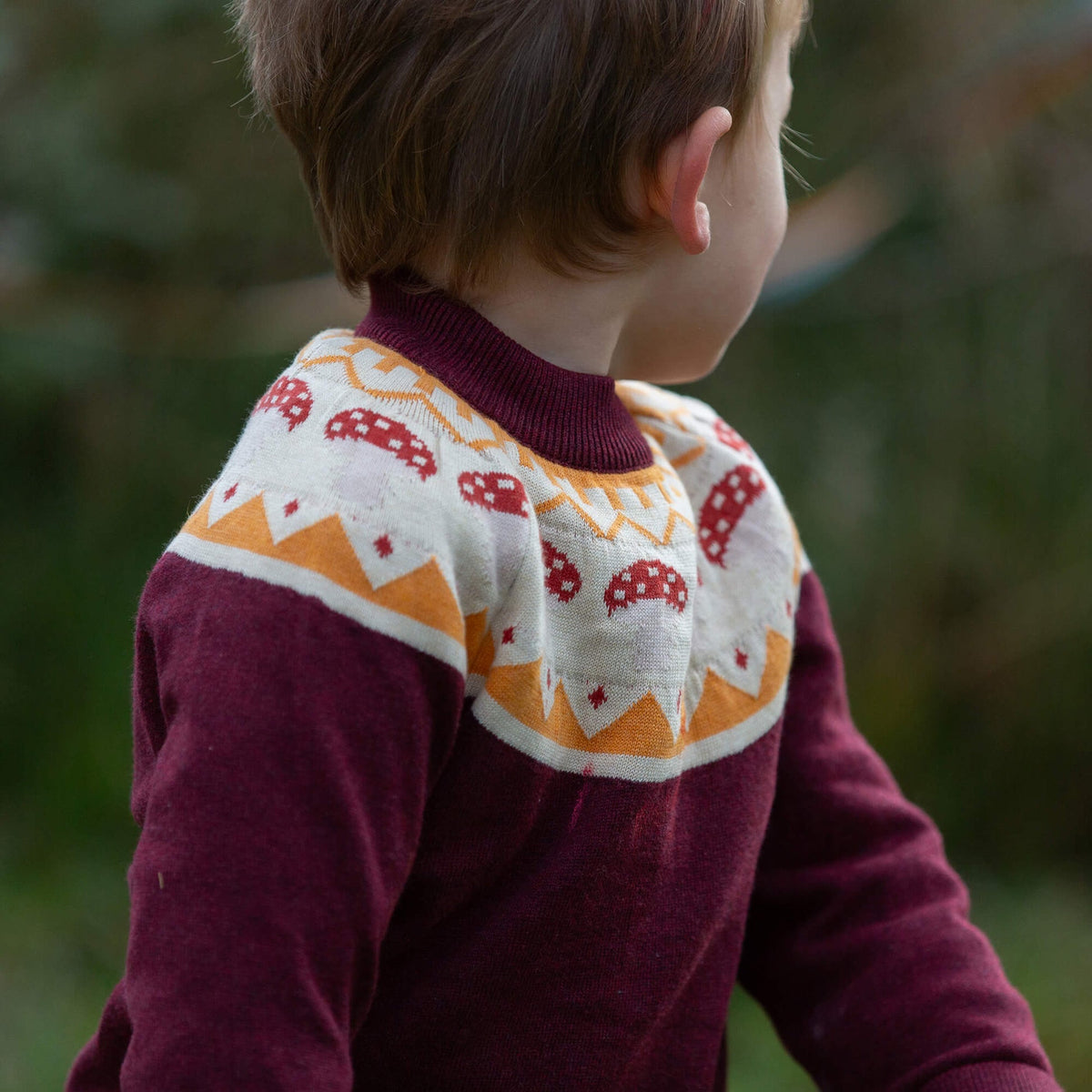 Child wearing a patterned sweater with a blurred natural background