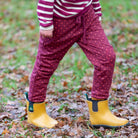 Person wearing maroon pants with red polka dots and yellow rain boots in a leafy outdoor setting