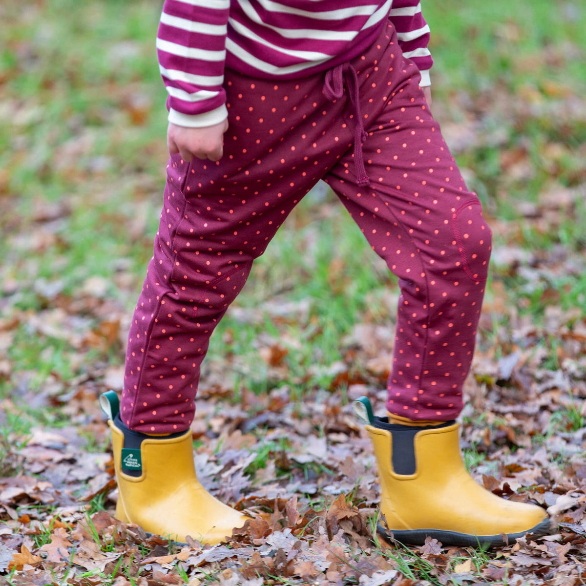 Person wearing maroon pants with red polka dots and yellow rain boots in a leafy outdoor setting