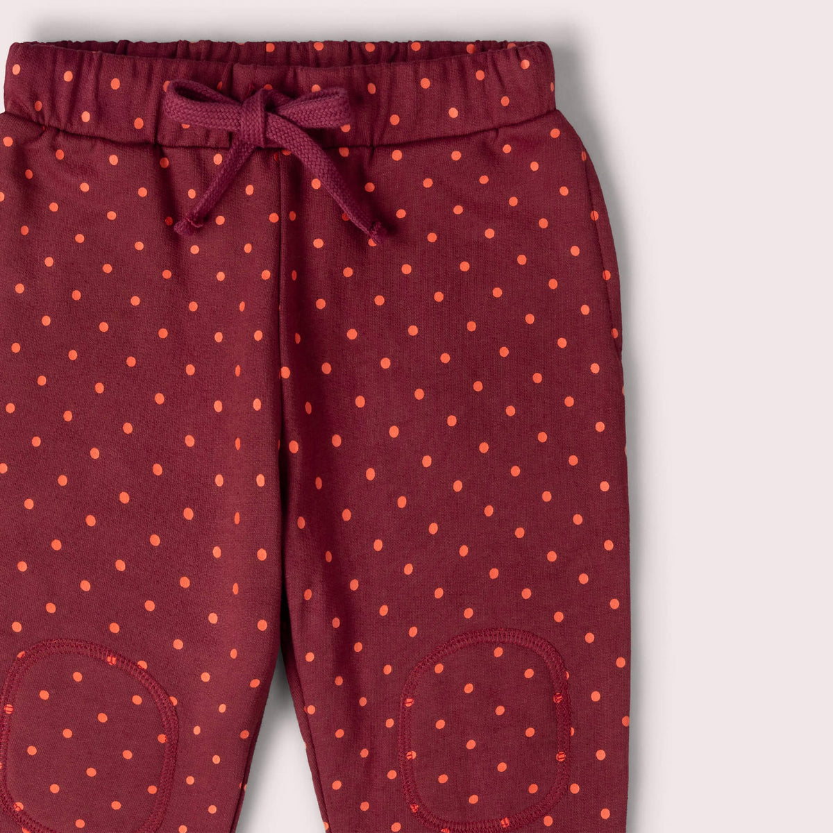 Maroon children's pants with orange polka dots and yellow cuffs on a white background
