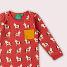 A red long-sleeve top with a repeating horse print and a mustard yellow chest pocket.