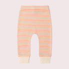 Baby pants with peach and cream horizontal stripes and solid cream ribbed cuffs, shown flat against a pale pink background.