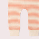 A close-up of striped baby pants with peach and cream horizontal stripes and solid cream ribbed cuffs, shown flat against a pale pink background.