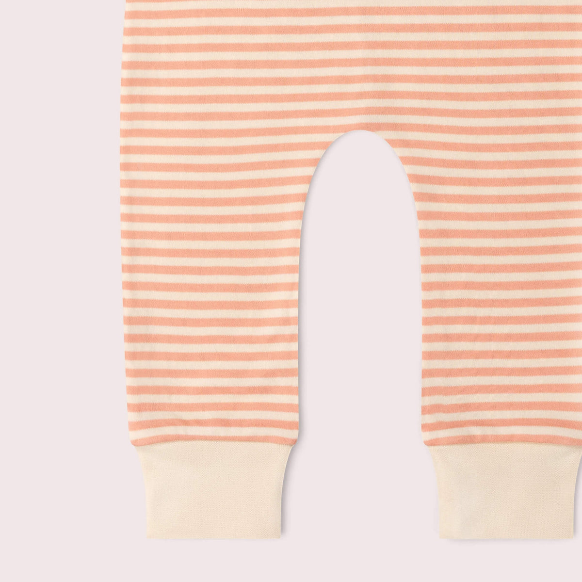 A close-up of striped baby pants with peach and cream horizontal stripes and solid cream ribbed cuffs, shown flat against a pale pink background.