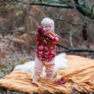 Child in pink outfit with animal patterns standing on a blanket in a forest setting