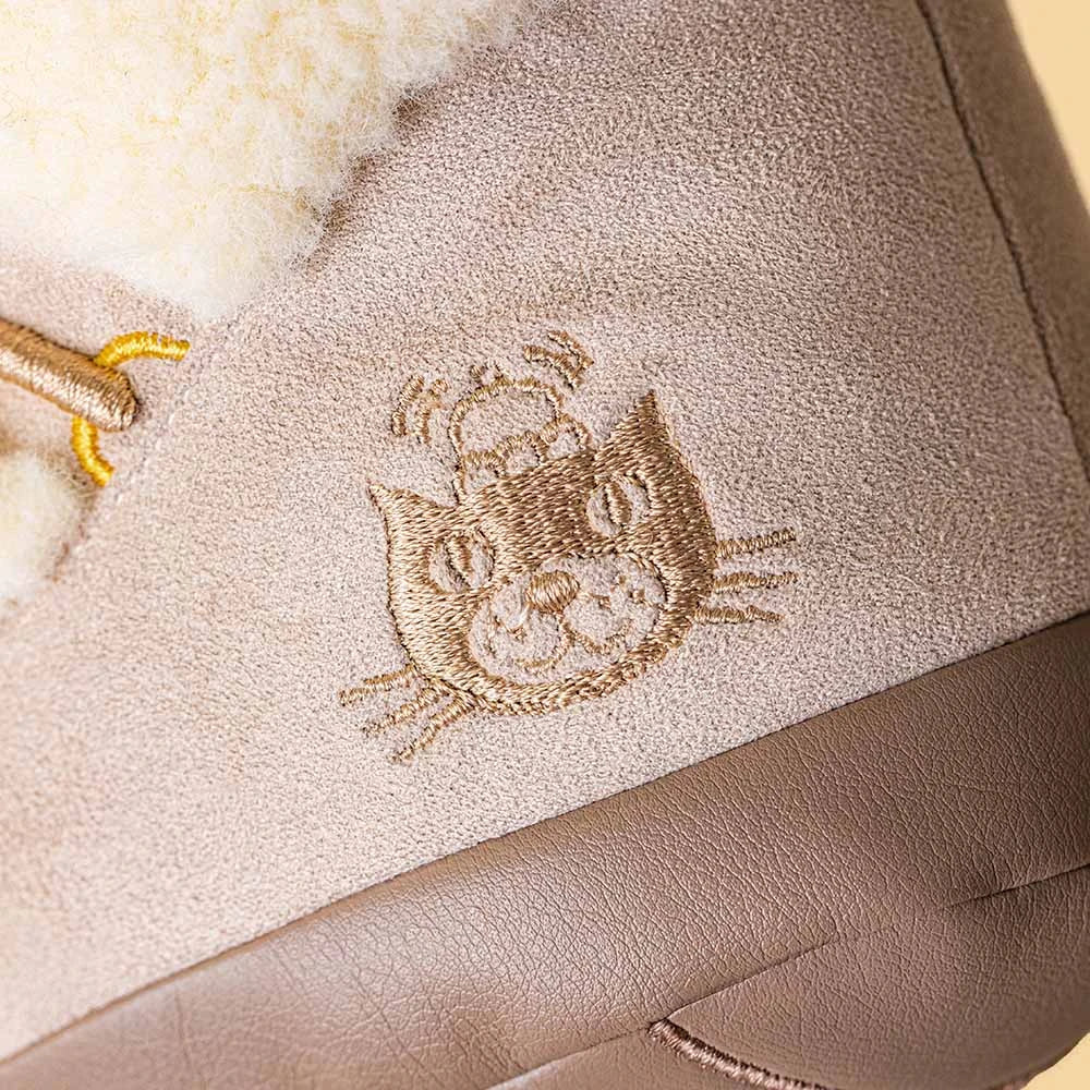 Close-up of a beige suede boot or shoe with a cream sherpa lining and an embroidered cat face on the side.