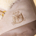 Close-up of a beige suede boot or shoe with a cream sherpa lining and an embroidered cat face on the side.