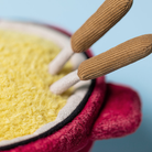 Close-up of a red pot with yellow contents and wooden sticks on a blue background