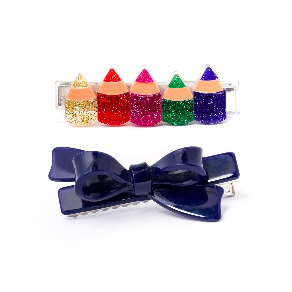 Two hair clips on a white background: a large glossy navy blue bow clip in front, and a clear barrette clip behind holding five glitter pencil-shaped charms in gold, red, pink, green, and purple.