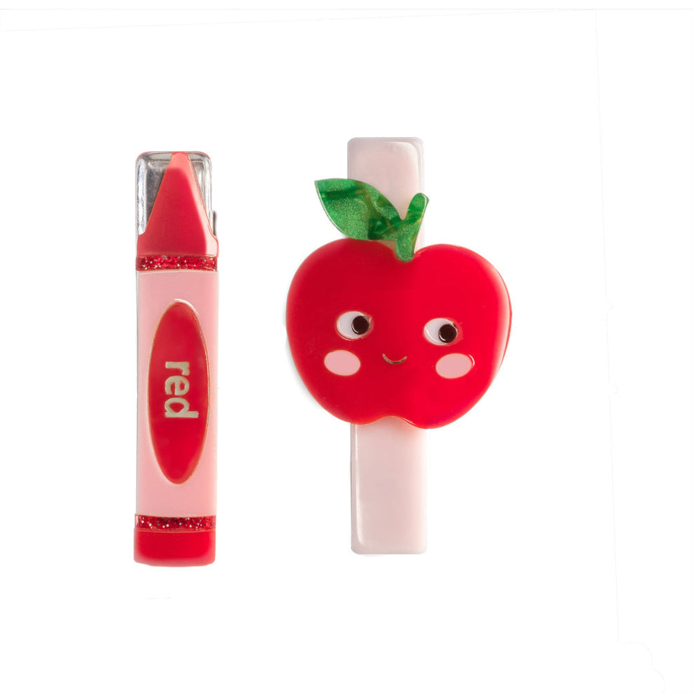 A red crayon-shaped lip gloss tube and a red apple-shaped hair clip, both with cute cartoon faces, displayed on a clean white background.