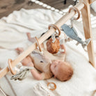 Baby lying on a blanket with a wooden play gym and hanging toys