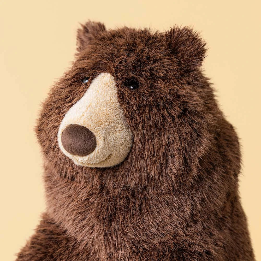 A close-up of a brown plush bear toy with a cream-colored snout and dark eyes, set against a solid pale yellow background.