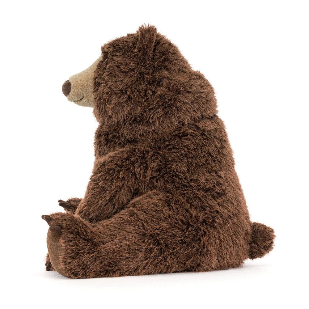 A plush brown bear toy sitting upright, photographed from the side against a clean white background.