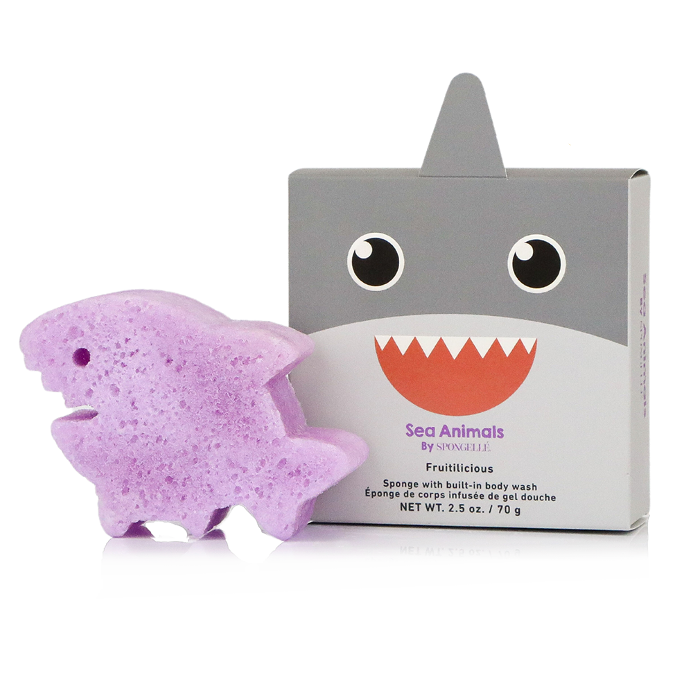 A purple shark-shaped sponge body wash sponge displayed next to its gray and white retail box featuring a cartoon shark face. The box is labeled 'Sea Animals by O'NeeLoo' and 'Fruitylicious'.