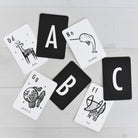 seven black and white cards showing letters and animals on a textured white wood background