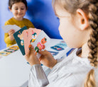 Children playing with colorful cards at a table against a blue wall.