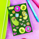 Sheet of pickle-themed stickers on a colorful background with pens.