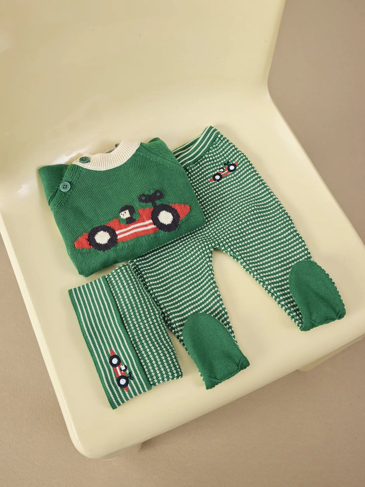 Green baby outfit with car design on a beige surface