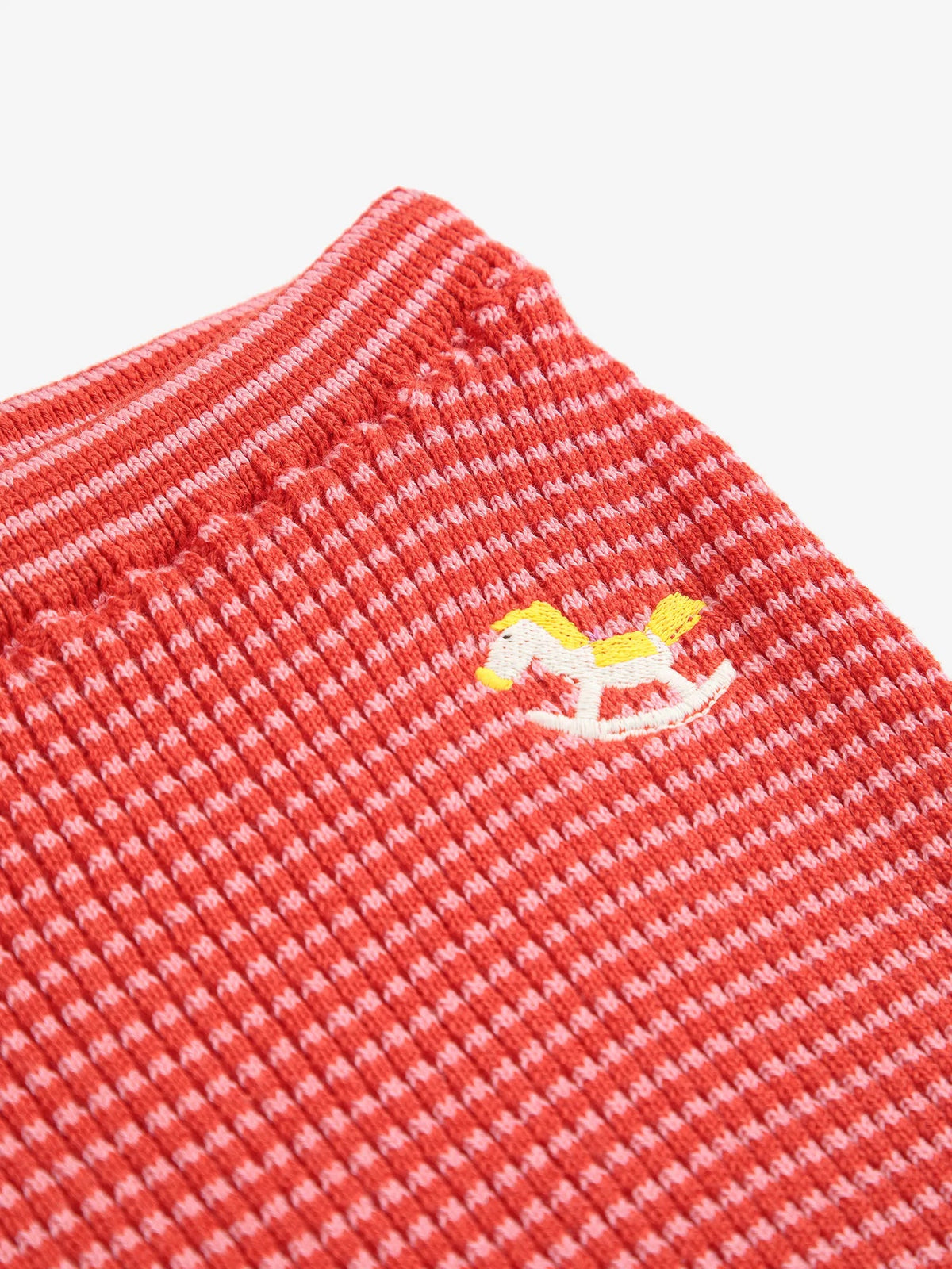 Close-up of a red textured fabric with a small embroidered rocking horse design on a white background