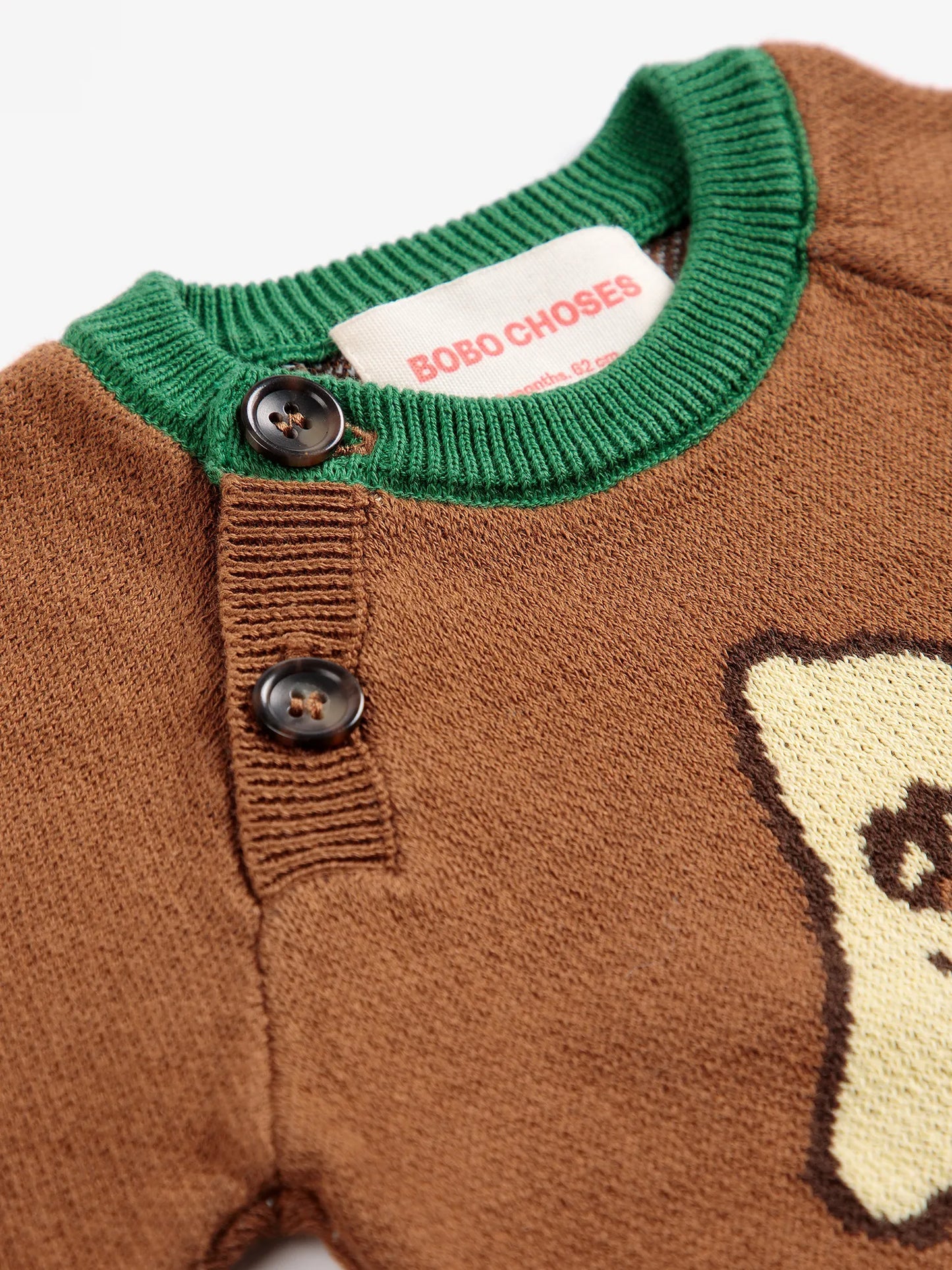 Close-up of a brown knit sweater with a green ribbed collar, two dark buttons, and a visible BOBO CHOSES neck label.
