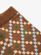 Close-up of a brown knit garment, likely a sweater or scarf, featuring a diamond argyle pattern in light blue, pale yellow, and green, with a ribbed brown collar.