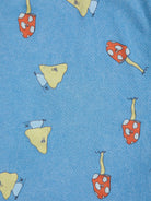 A close-up of a blue fabric surface printed with whimsical mushroom motifs in red, yellow, and light blue.