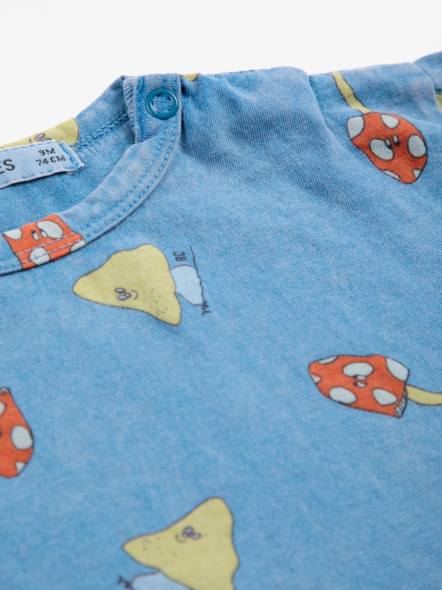 Close-up of blue fabric with cartoon mushroom patterns and a button.