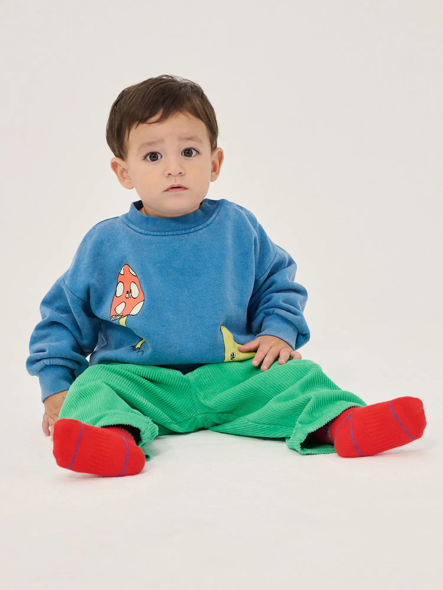 Child wearing a blue sweater with cartoon characters, green pants, and red socks on a white background