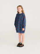 Young girl wearing a blue dress with red and green patterns on a white background