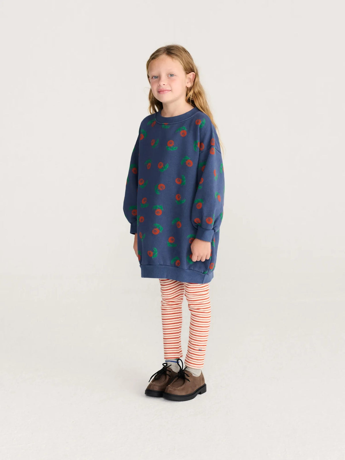 Young girl wearing a blue dress with red and green patterns on a white background
