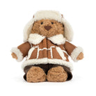 A plush teddy bear wearing a brown faux-leather aviator-style jacket with white faux-fur trim, a matching white aviator hat, and dark brown pants, photographed on a clean white background.
