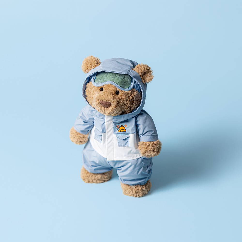 Teddy bear wearing a blue snowsuit with goggles on a light blue background