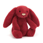 A plush red bunny stuffed animal with long floppy ears, small black eyes, and a small beige nose, photographed on a clean white background.